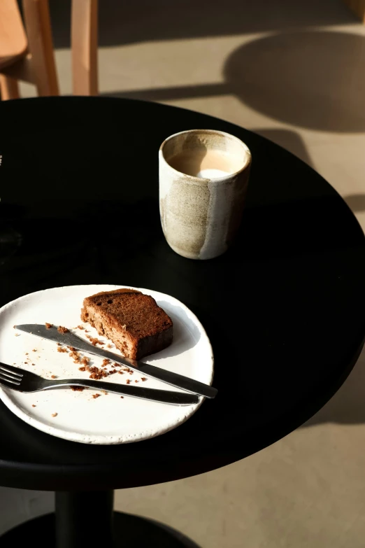 some brown stuff on a white plate next to some fork and coffee