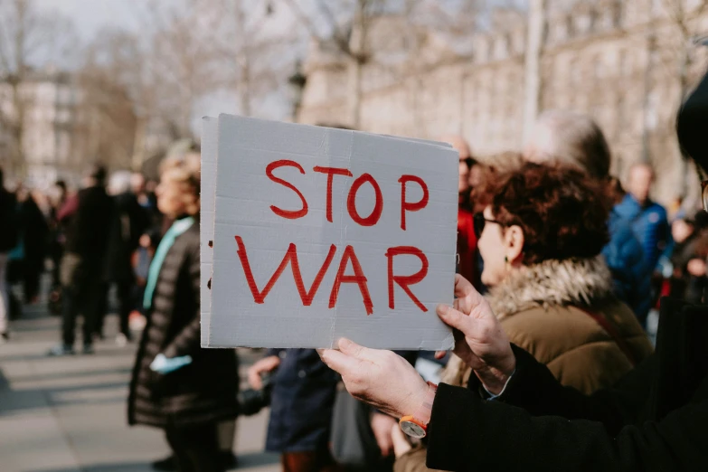 a woman is holding up a sign with the words stop war on it