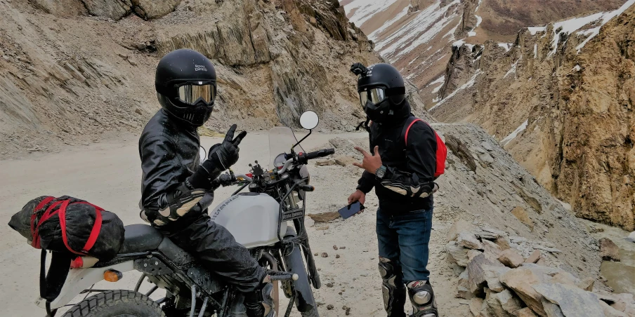 two men standing near a motorcycle on a trail