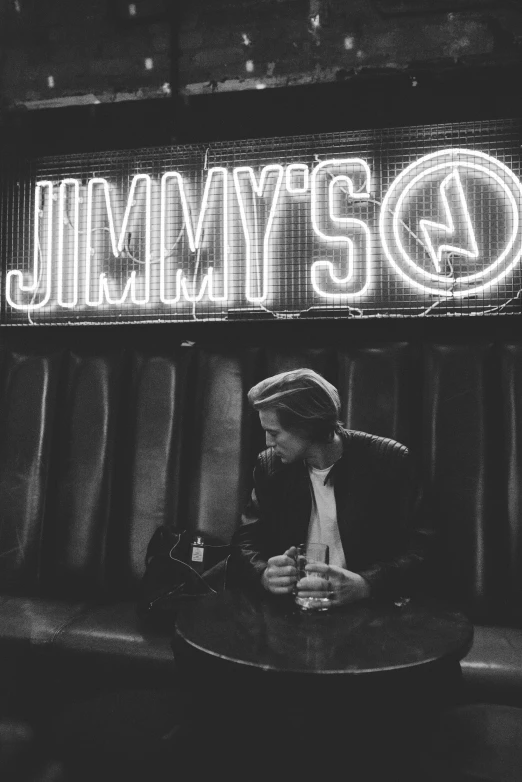 a man sitting at a table with a lit up sign in the background