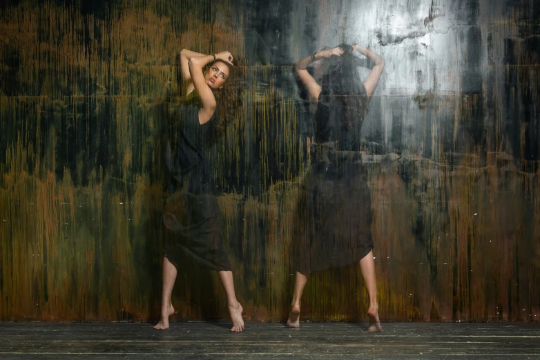 two women stand in front of a black curtain, and one has her hands on her head