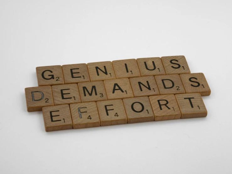 two pieces of scrabble are stacked up with words spelling genius, demands, effort