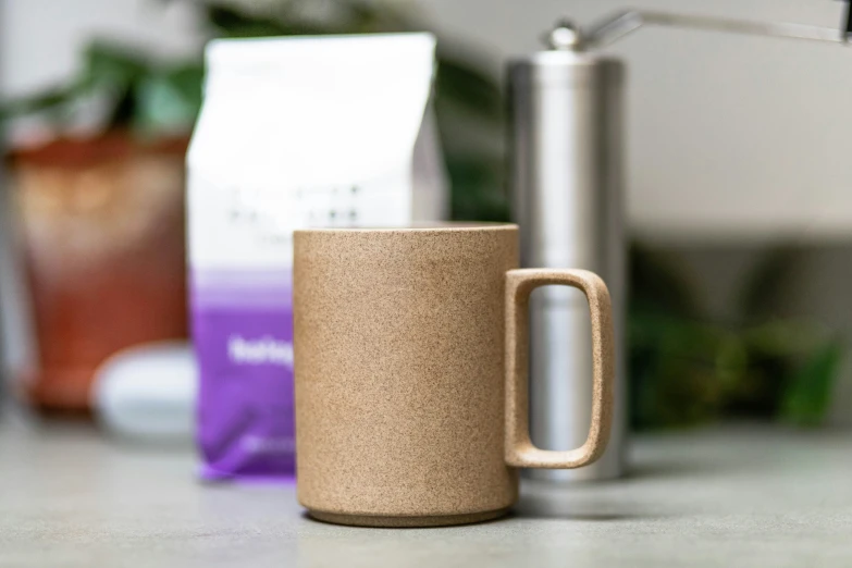 a tan mug is on a counter near a coffee cup