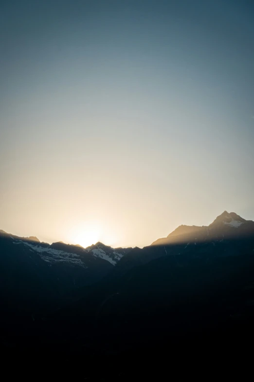 the sun rises over a mountain range with distant hills