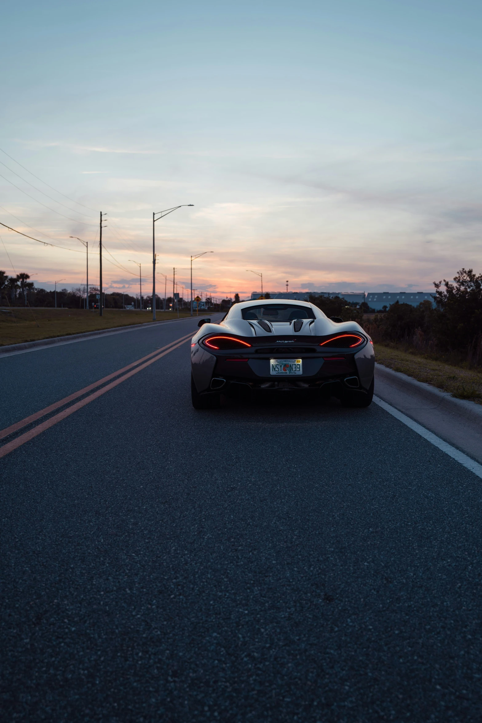 a silver car driving down the road at sunset