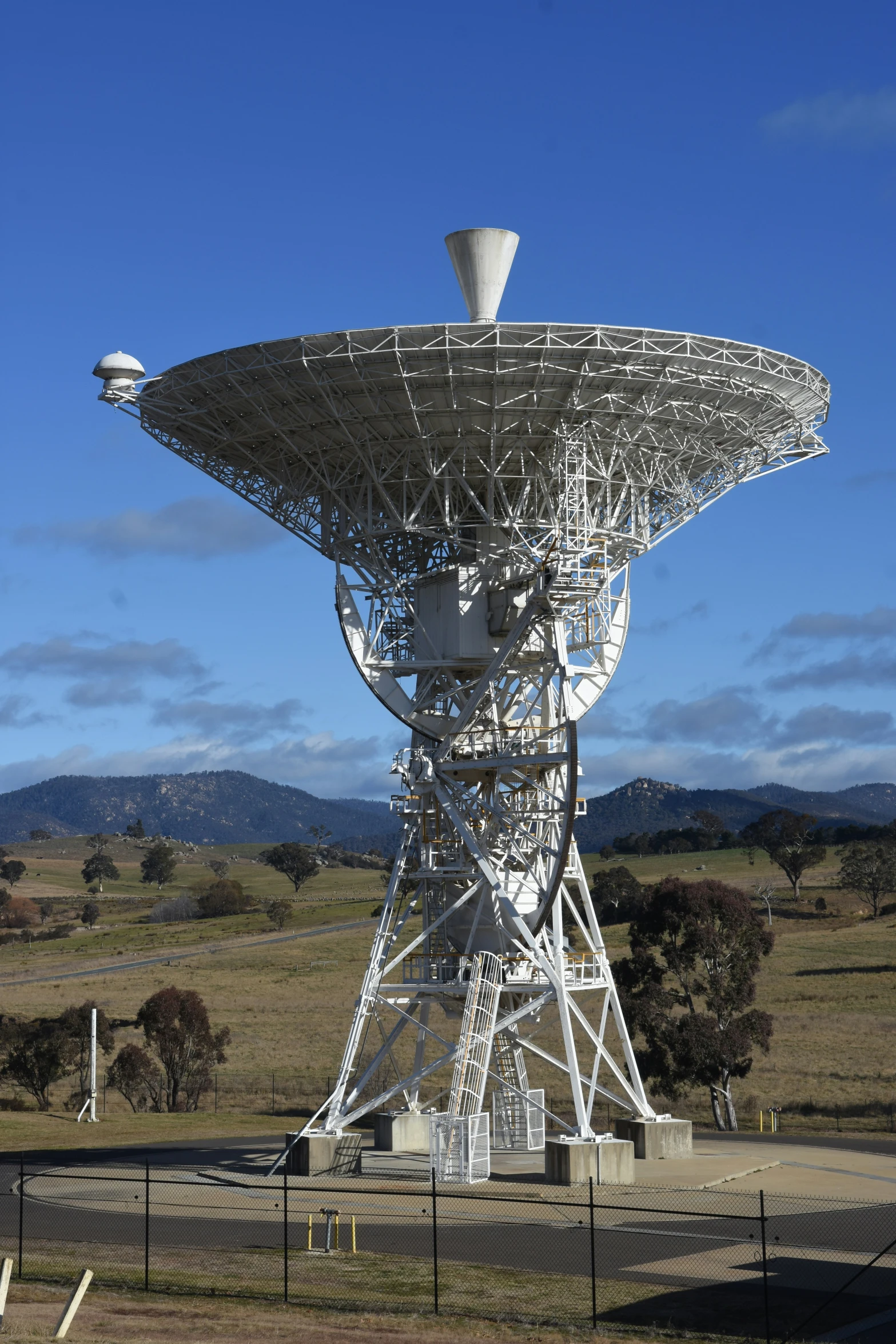 a large radio telescope near a fence and grassy field