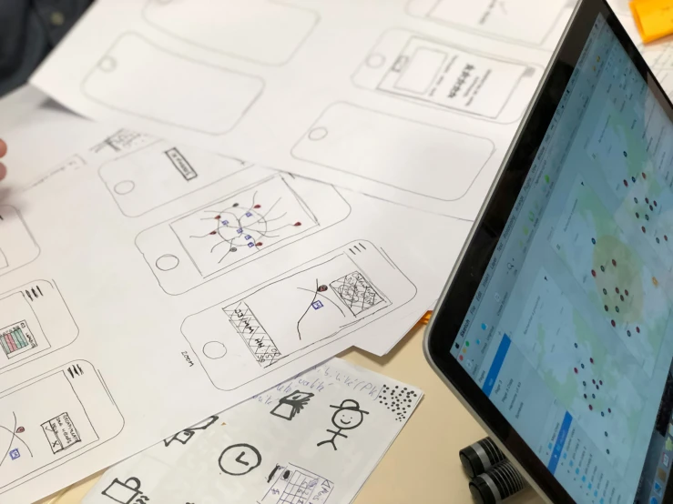 an ipad next to a paper that shows a computer and various drawings