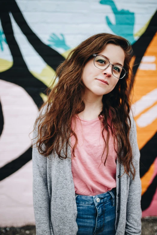 a girl with glasses standing in front of a mural