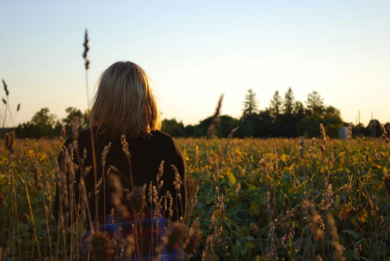 a girl standing in the middle of a field with tall grass