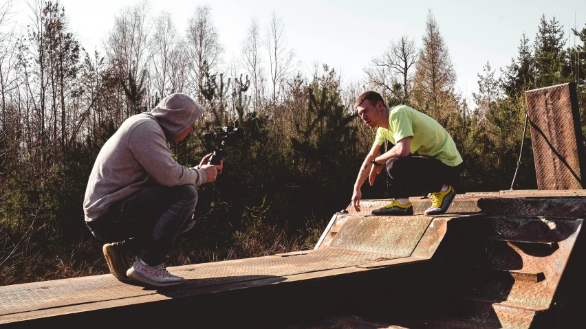 two men are sitting down on wooden structures while another man is holding a camera