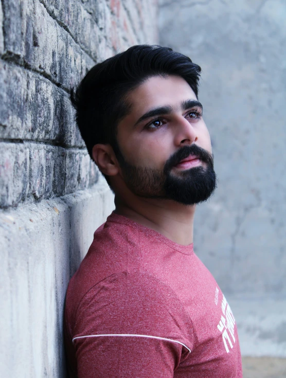 a man with beards and a red shirt near a wall