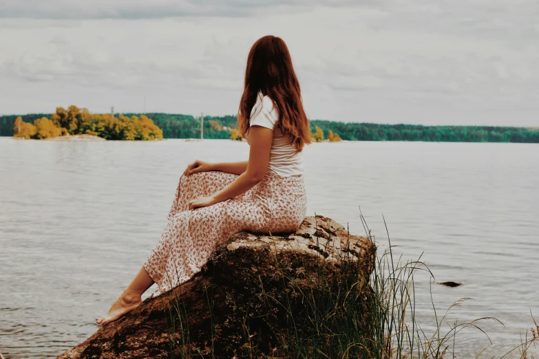 a woman sitting on top of a rock next to a lake