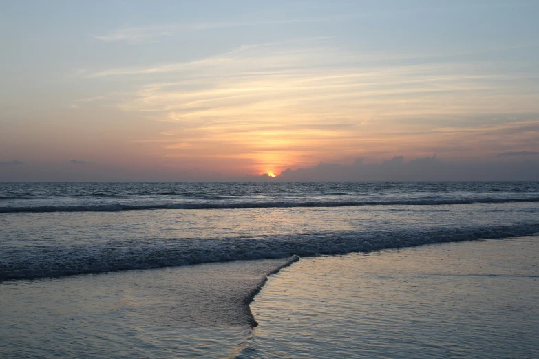 the sun setting over the ocean with some waves on shore