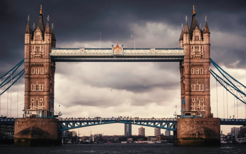 a very tall bridge on the river under cloudy skies