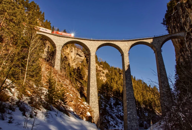 the train is crossing the high bridge that runs over the mountain