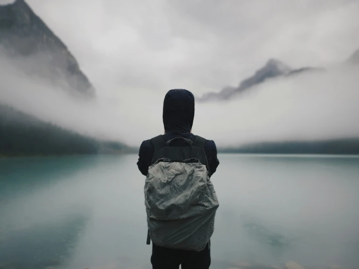 the man is standing in front of a body of water with mountains on either side