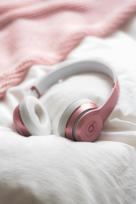 a pair of pink and white headphones lie atop a blanket