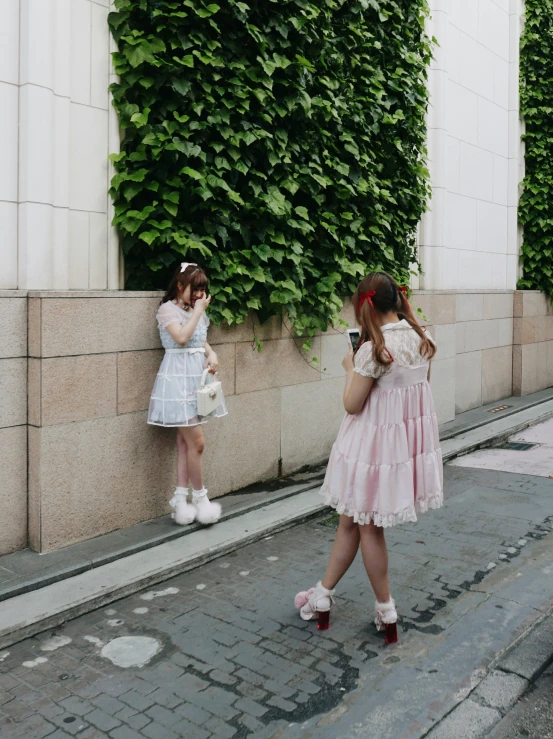 a woman taking a pograph of another woman wearing a short pink dress and boots on a city street