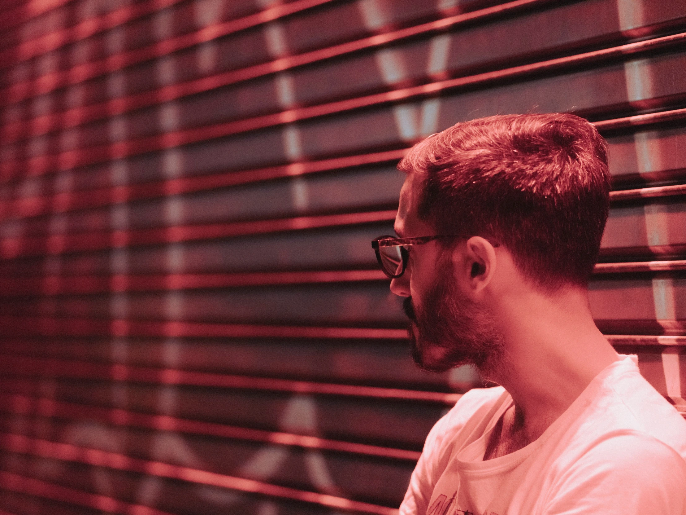 the man has on a white shirt and glasses looking at a red background