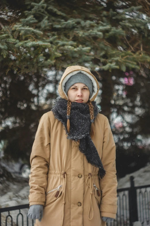 woman in tan coat and black scarf with a tree in the background