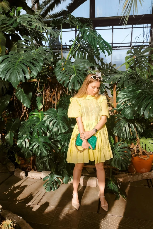 a young woman in a dress standing by a plant