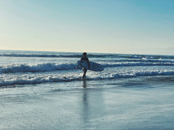 a surfer holding his surfboard walking along the beach