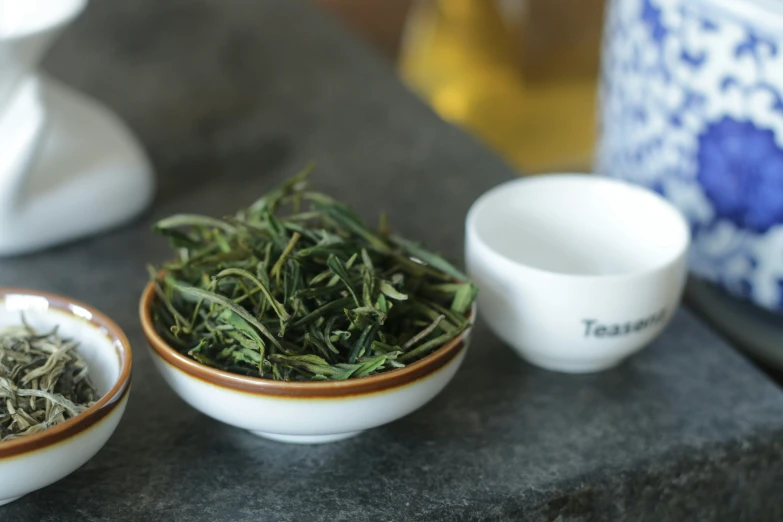 three white bowls filled with green leaves near two mugs