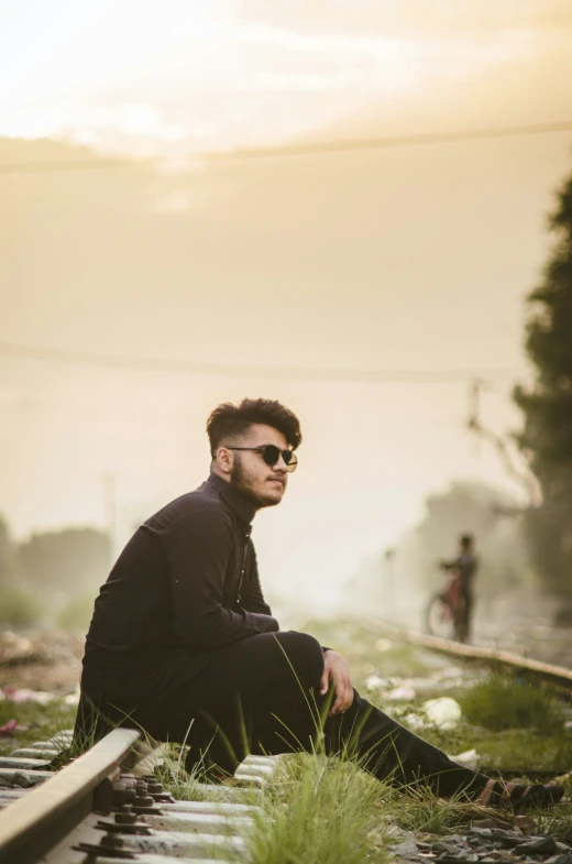 the man is sitting on railroad tracks near tall grass