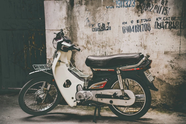 a white scooter parked in front of a wall with a graffiti on it