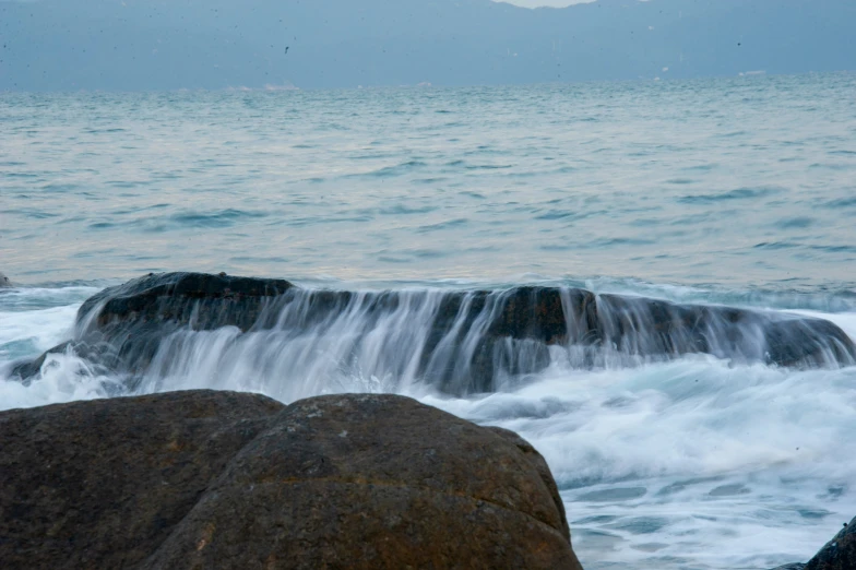 a rocky coast is covered in waves with a bird perched atop