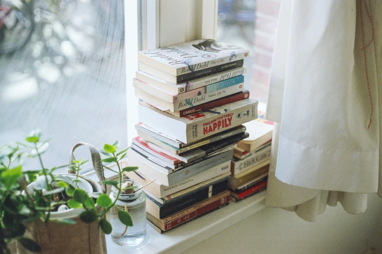 stack of books sitting on a windowsill next to a window