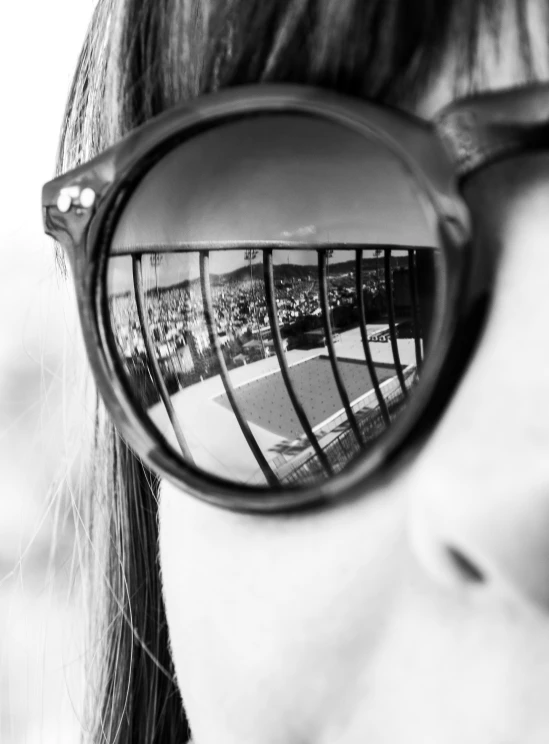 a girl with glasses that have reflection of some tennis courts in them