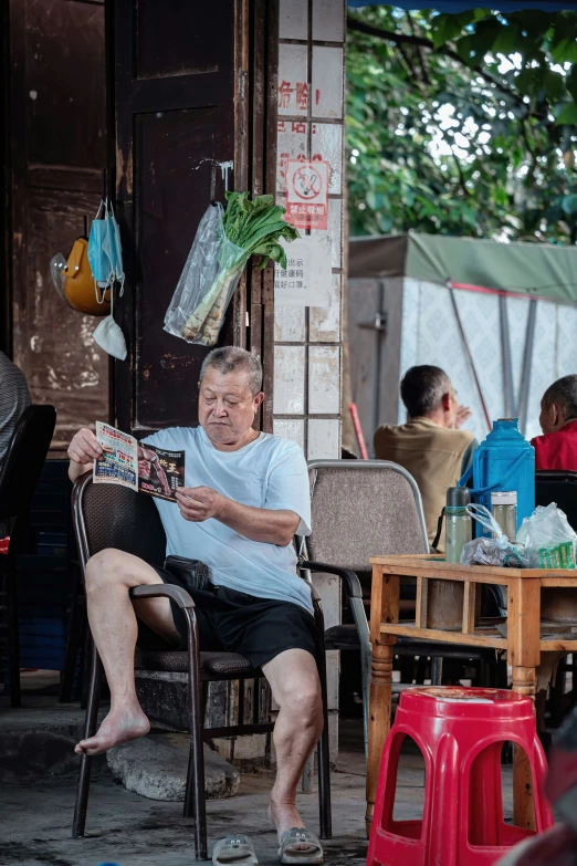 an elderly man sits in his patio chair looking at a newspaper