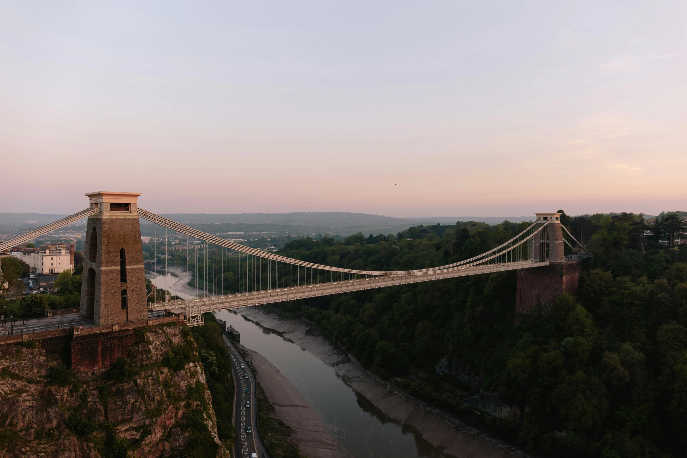 the suspension bridge spans over a river at sunset