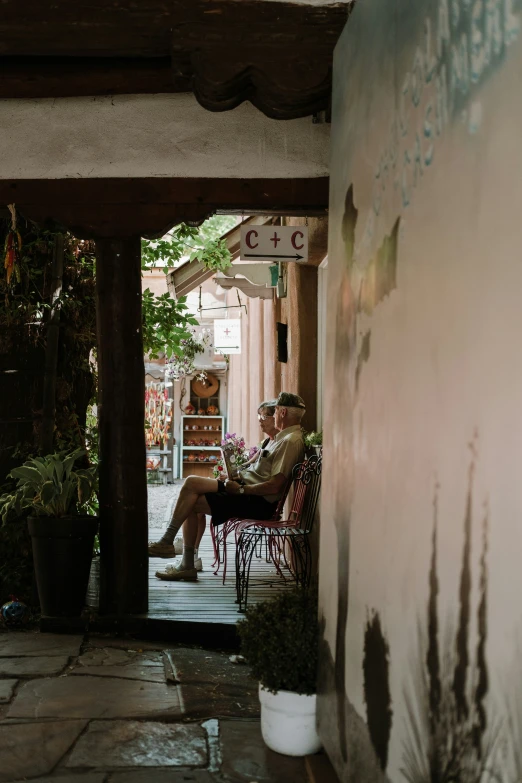 a man sitting on a chair next to a wall in front of a potted plant