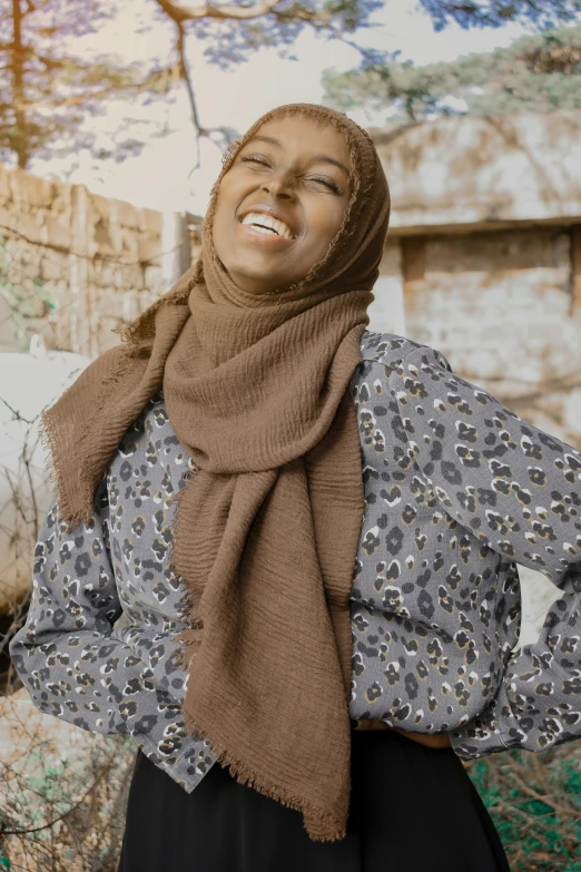 a woman with a headscarf smiles as she stands in front of trees