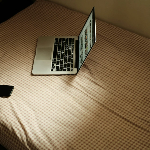 an open laptop and a phone sitting on top of a bed