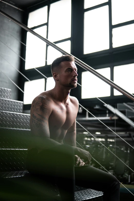 a shirtless man sits on a bench beneath a large window