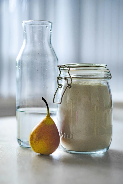 a bottle and bowl on a table with a single pear next to it