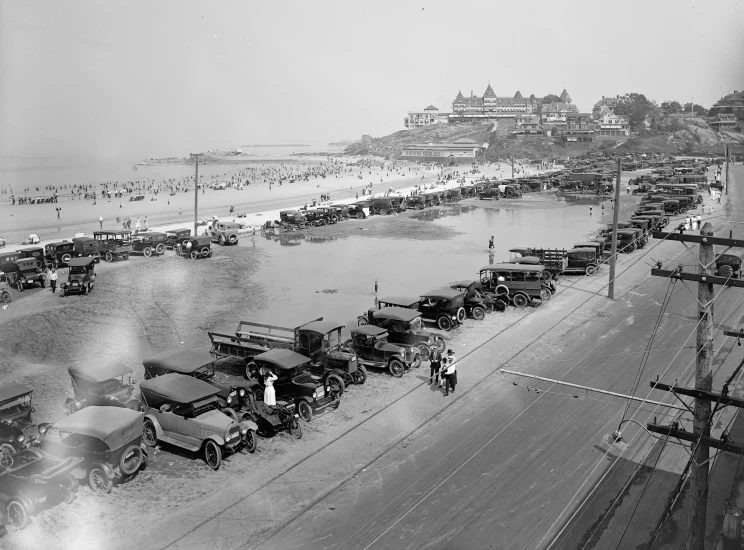 a black and white po of a beach with cars and people