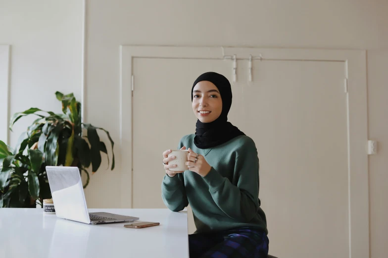 a woman in a headscarf sitting at a desk with her hands clasped