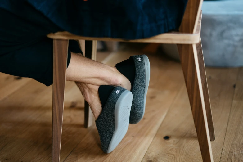 a person sitting under a chair with a leg and a pair of shoes