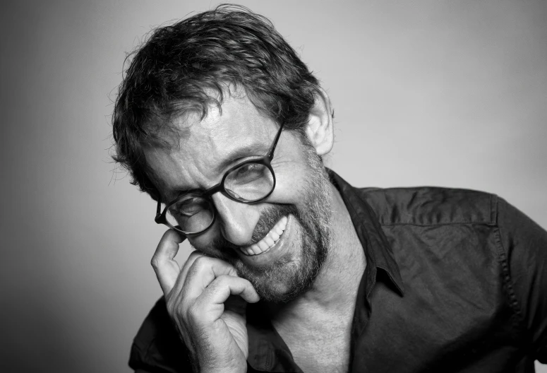 man with glasses smiling while leaning his head against a wall
