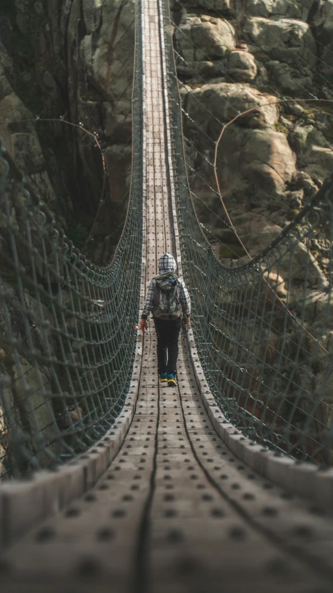 a person walks across a suspension bridge between the rocks