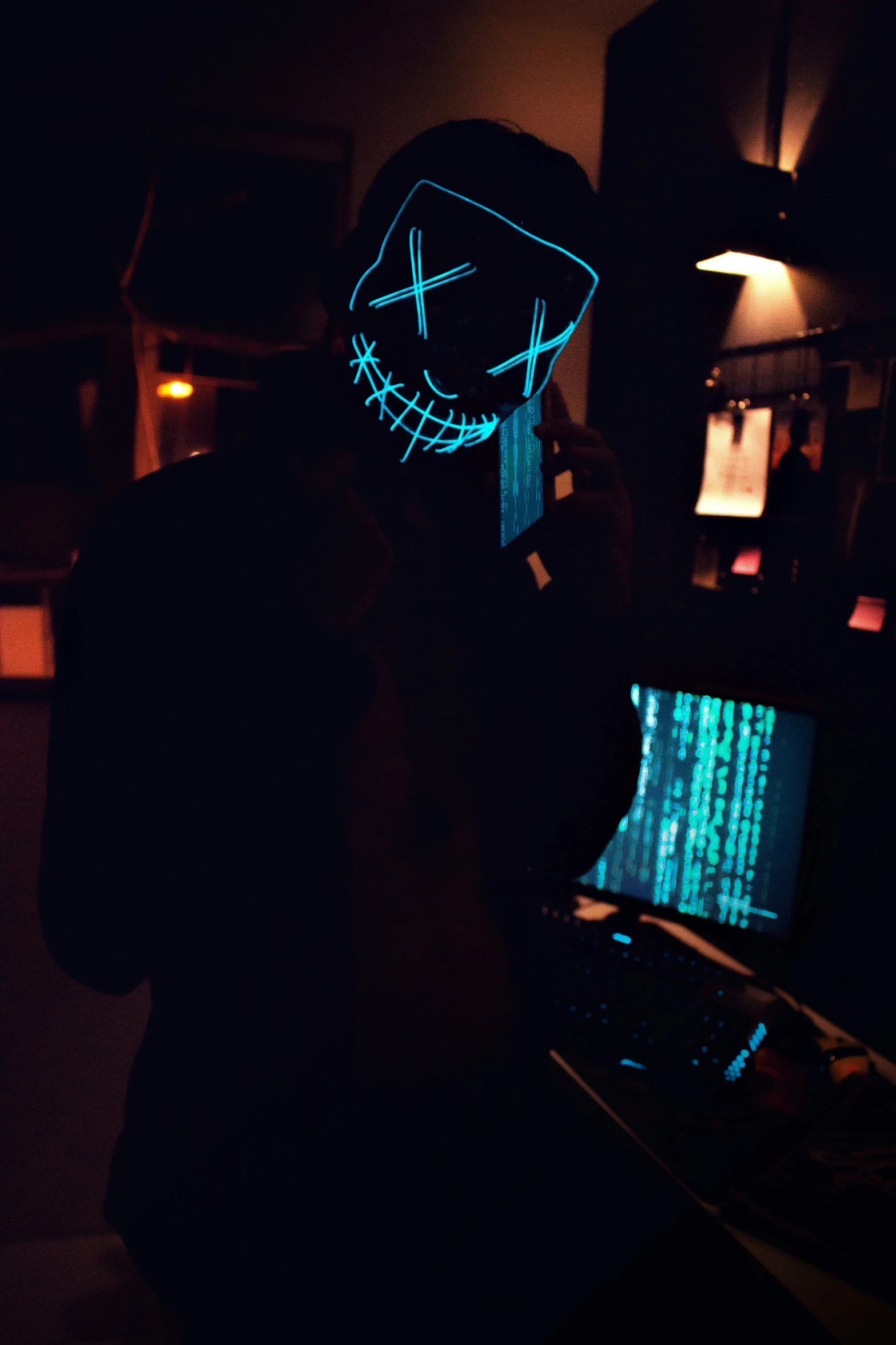 someone wearing a glowing mask next to two computers