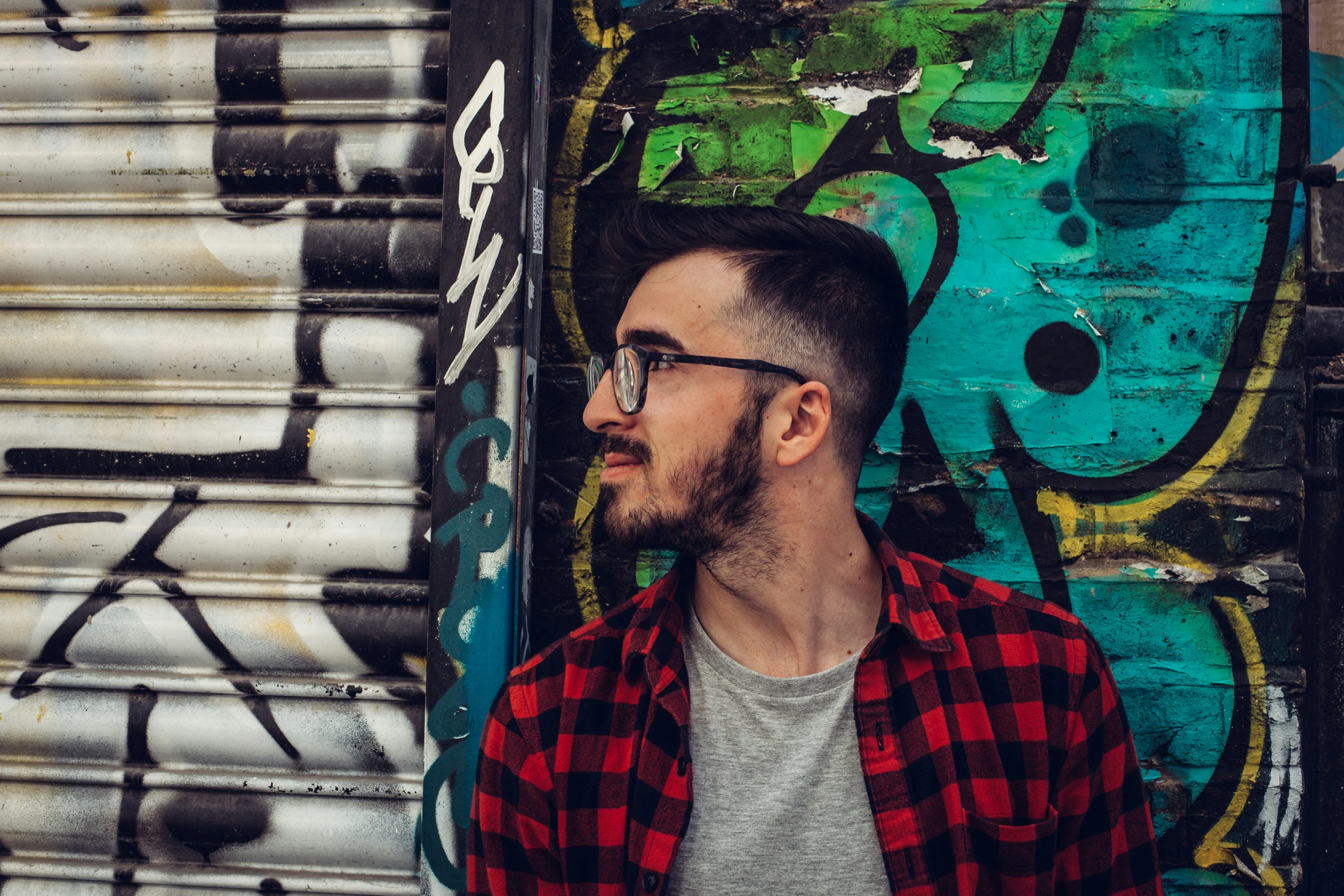 a man wearing glasses standing against a wall