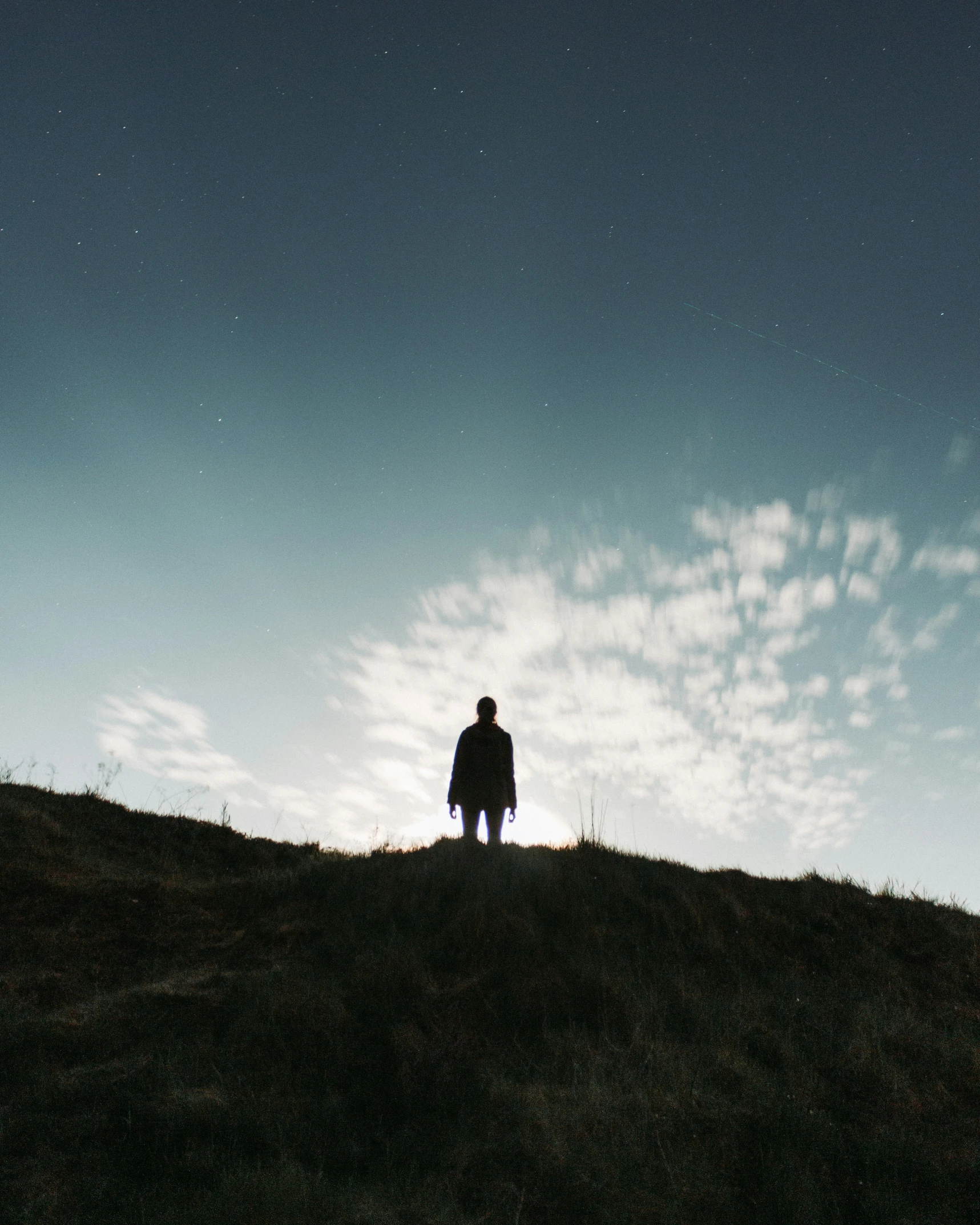 a person standing on top of a hill under a cloud covered sky