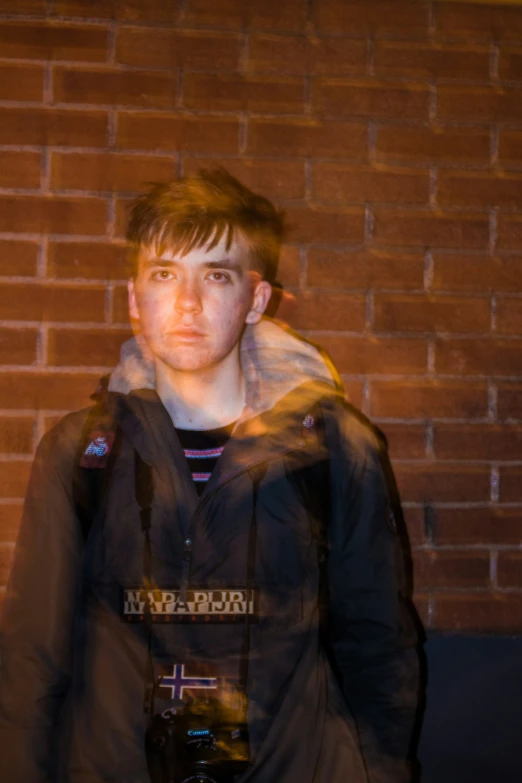 young man standing in front of a brick wall in the sun