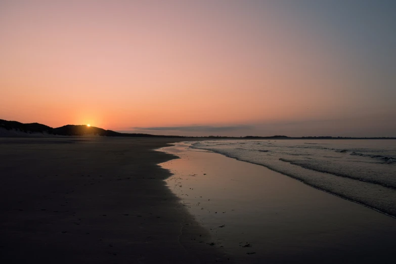 the sun rises on the horizon, near a sandy beach