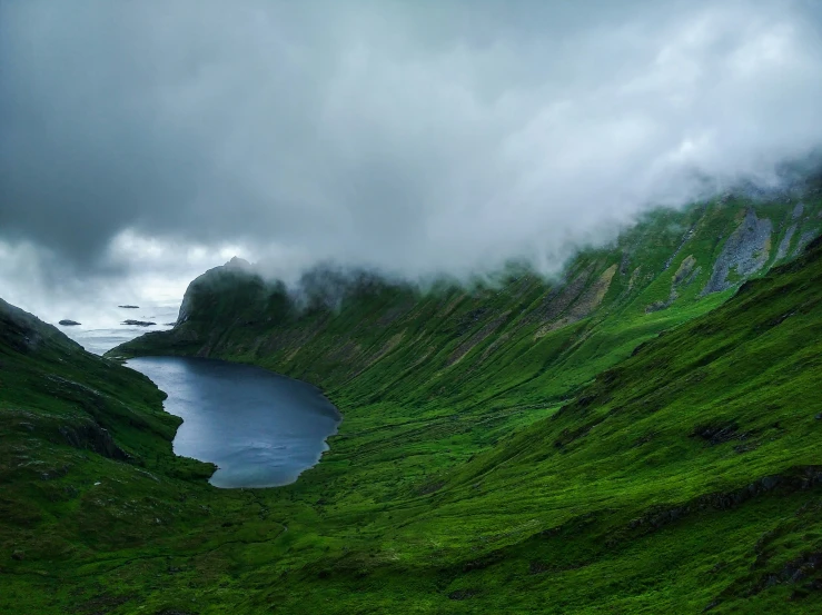 a cloudy day with fog hovering above the water and green hilly terrain